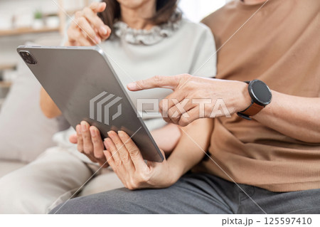Elderly Couple Relaxing on Sofa with Tablet in Cozy Living Room Setting, Enjoying Leisure Time Together in Comfortable Home Environment 125597410