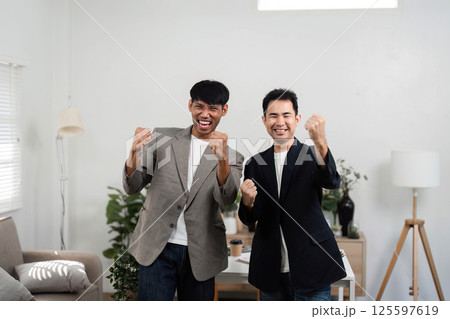 Celebration and Team Spirit in Business. Two men expressing excitement in a modern office, showcasing their teamwork and success. Celebration and Team Spirit in Business. Two men expressing excitement in a modern office, showcasing their teamwork and success. 125597619