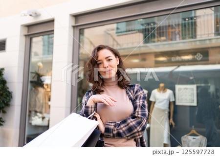 Stylish woman with shopping bags walking outside a fashion boutique, enjoying a shopping day in the city. 125597728