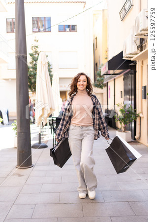 Stylish woman with shopping bags walking outside a fashion boutique, enjoying a shopping day in the city. 125597759