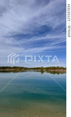 Tranquil lake reflecting blue sky and clouds with serene nature landscape view concept Tranquil lake reflecting blue sky and clouds with serene nature landscape view concept 125597834