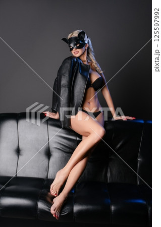 Woman in lingerie poses on a black leather couch with a playful mask 125597992