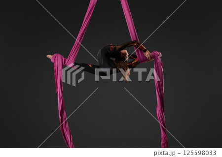 Girl performs aerial gymnastics using pink fabric suspended from a pole Girl performs aerial gymnastics using pink fabric suspended from a pole 125598033