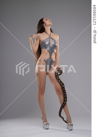 Elegant woman poses with a snake while wearing striking lingerie in a studio 125598084