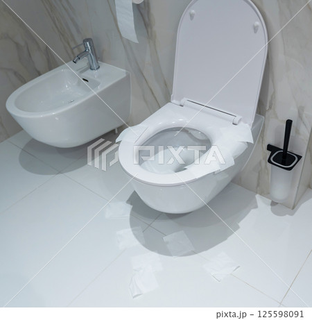 A white public toilet with paper-lined seat and scattered tissue on floor A white public toilet with paper-lined seat and scattered tissue on floor 125598091