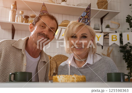 Senior couple wearing party hats celebrating birthday with cake at home 125598363