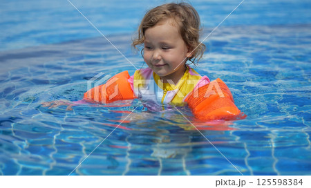 Little girl learning to swim with armbands in a pool Little girl learning to swim with armbands in a pool 125598384