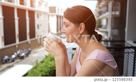 Woman takes cup of coffee enjoying cityscape from balcony 125598393