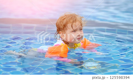 Cute baby girl learning to swim with armbands in pool 125598394