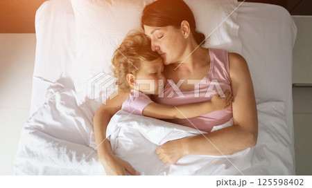 Mother and daughter sleeping peacefully embracing in hotel bed 125598402