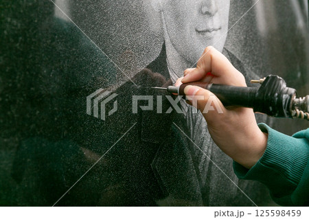 The hand of a female artist who applies images to monuments by hand engraving. 125598459