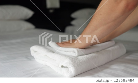 Woman housemaid puts clean towels onto bed with bedclothes 125598494
