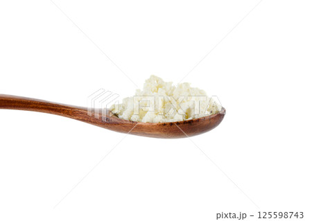 Close-up of crumbly cottage cheese on a wooden spoon on a white background. 125598743