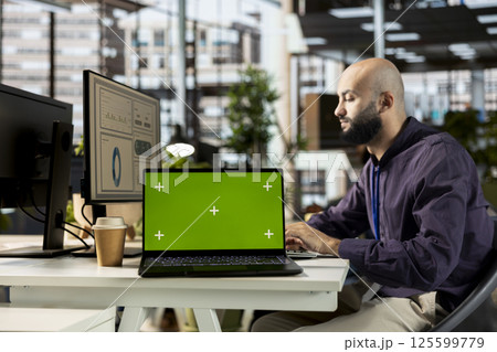 Young middle eastern advisor handling financial reports next to isolated screen, verifying business data in order to increase funds. Male worker using his expertise to solve administrative tasks. 125599779