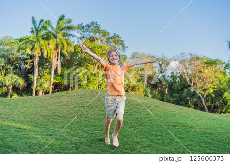 Boy wearing a pilot hat running through the grass with a toy airplane, dreaming of adventures. Childhood, imagination, and freedom concept 125600373
