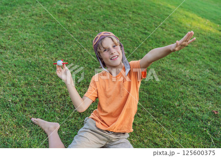 Boy wearing a pilot hat running through the grass with a toy airplane, dreaming of adventures. Childhood, imagination, and freedom concept Boy wearing a pilot hat running through the grass with a toy airplane, dreaming of adventures. Childhood, imagination, and freedom concept 125600375