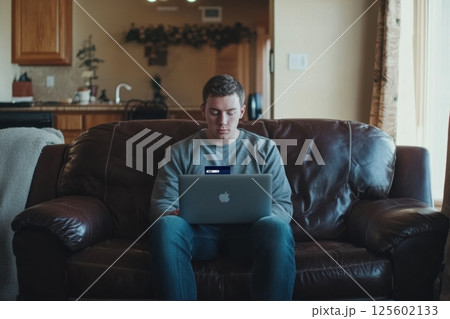 Young man sitting on couch working on laptop in cozy living room during daytime 125602133