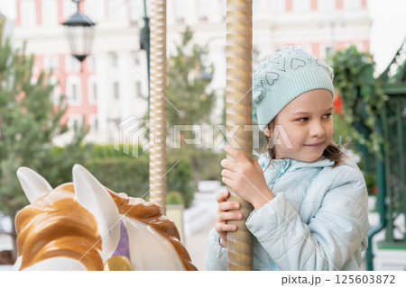 Little happy cute girl riding on carousel horse in park. Little girl have fun on carousel. 125603872