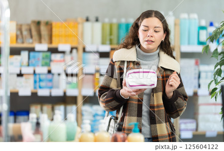 Young woman chooses feminine pads at pharmacy 125604122