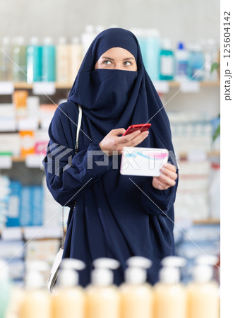 Young woman in hijab scans qr code of pills 125604142