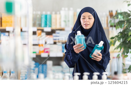 Female customer in Islamic clothing comparing two mouthwash products at drugstore 125604215
