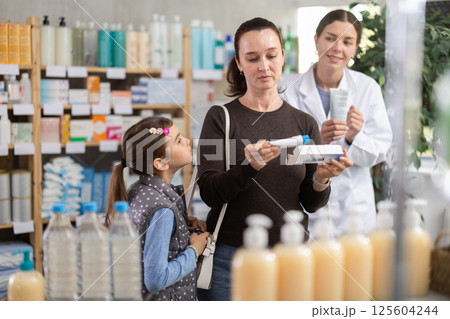Middle-aged woman with daughter choosing ointment in drugstore Middle-aged woman with daughter choosing ointment in drugstore 125604244