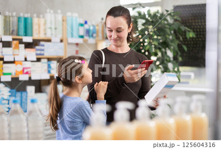 Woman with daughter in pharmacy scans QR code on cream 125604316