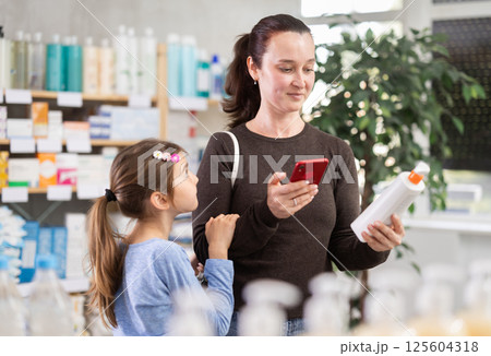 woman with a child pays for purchases using a QR code at a pharmacy 125604318