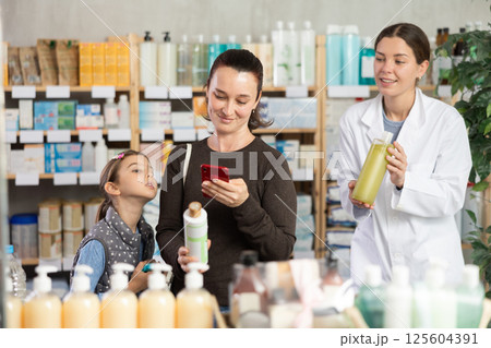 Middle-aged woman with daughter scanning barcode on shampoo in drugstore Middle-aged woman with daughter scanning barcode on shampoo in drugstore 125604391