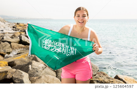 Young woman on coast posing with flag of Saudi Arabia Young woman on coast posing with flag of Saudi Arabia 125604597