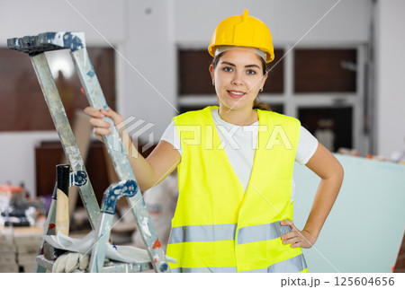 Portrait of female foreman in protective yellow vest and hard hat in room being renovated 125604656