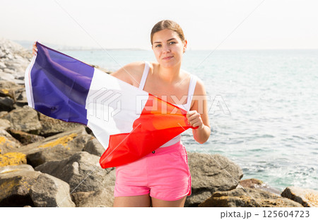 Young happy woman holding flag of French with a happy face and smiling on seashore on sunny day 125604723