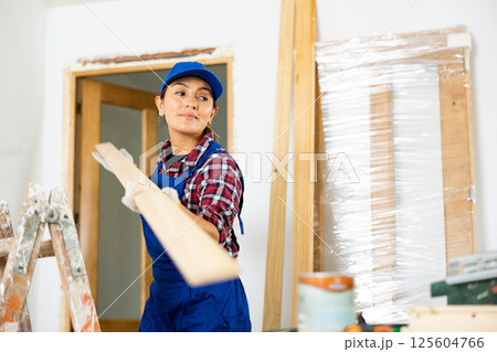 Cheerful female repairer carrying bunch of wooden planks 125604766
