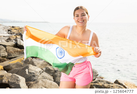 Pretty young girl holding the India flag in her hands on the beach on sunny day 125604777