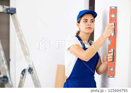 Woman worker measuring wall with spirit level 125604795