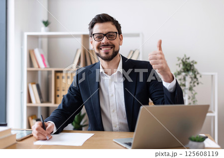 Professional adult male wearing suit working at desk smiling showing approval gesture thumbs up 125608119