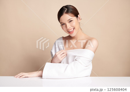 A beautiful young Asian woman with clean, fresh skin against a beige background. Skincare, facial treatment, cosmetology, beauty, and spa. An elegant portrait of an Asian woman. 125608404