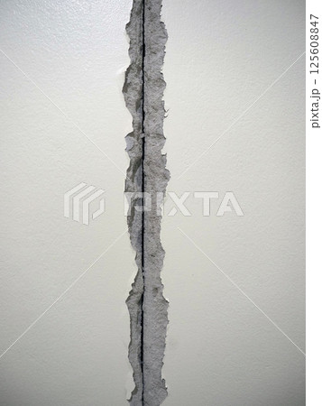 A damaged wall with visible crack, showing torn paper and exposed surface underneath, creating distressed appearance 125608847