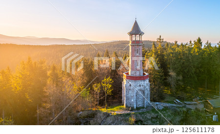Stepanka Lookout Tower stands tall in the Jizera Mountains during a serene spring morning. The surrounding trees bask in warm sunlight, creating a tranquil natural setting. 125611178