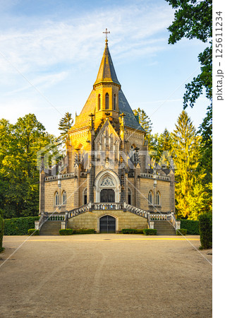 The Schwarzenberg Tomb, an ornate structure in Domanin, showcases Gothic architectural features surrounded by lush greenery, reflecting a serene atmosphere at dusk. 125611234