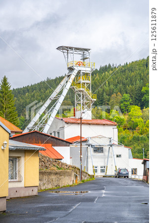The mining tower in Jachymov is a significant landmark, surrounded by a quaint neighborhood and lush green hills. It highlights the area's mining heritage and industrial history. 125611879