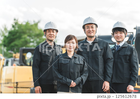 重機の前にいる作業着姿の建設業・建築業の作業員男女 重機の前にいる作業着姿の建設業・建築業の作業員男女 125612678