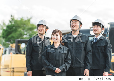 重機の前にいる作業着姿の建設業・建築業の作業員男女 重機の前にいる作業着姿の建設業・建築業の作業員男女 125612680