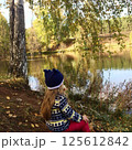 A little girl in a blue hat sits by the river looking at the water. 125612842