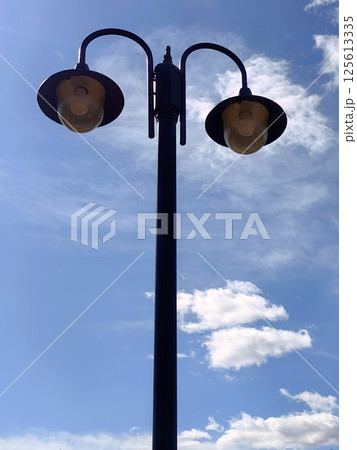 street lamp against blue sky with scattered clouds during sunny afternoon. close up. street lamp against blue sky with scattered clouds during sunny afternoon. close up. 125613335