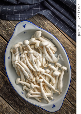 Raw white shimeji mushrooms in bowl on wooden table. Top view. Raw white shimeji mushrooms in bowl on wooden table. Top view. 125613507