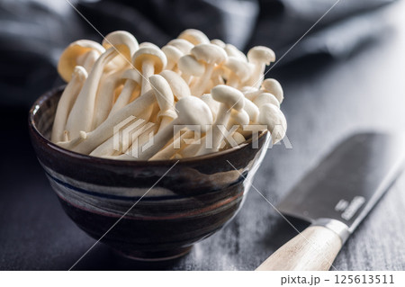 Raw white shimeji mushrooms in bowl on black table. Raw white shimeji mushrooms in bowl on black table. 125613511