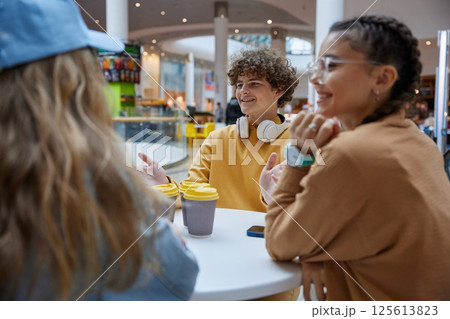 Happy relaxed teenage friends talking sitting in cafeteria of shopping mall Happy relaxed teenage friends talking sitting in cafeteria of shopping mall 125613823