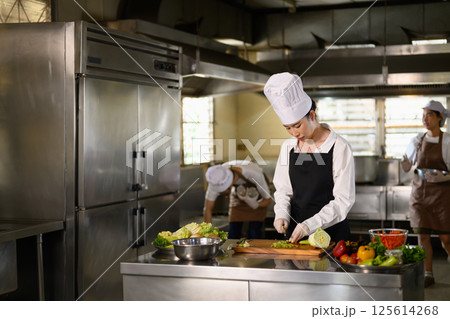 Focused culinary student preparing ingredients during a cooking class 125614268