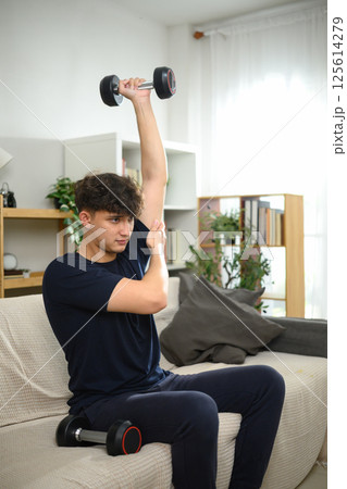 Young man exercising with dumbbells on sofa. Healthy lifestyle and home workouts 125614279